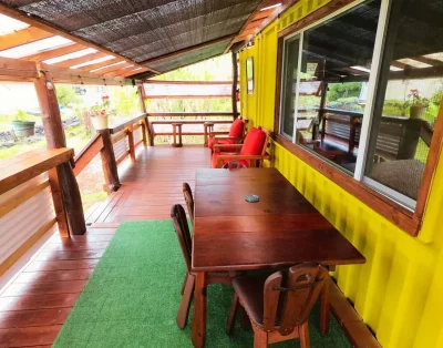 Deck area, with wooden dining table and comfortable deck chairs, of the tiny eco-friendly vacation rental at Da Fire Farm in Volcano, Hawaii